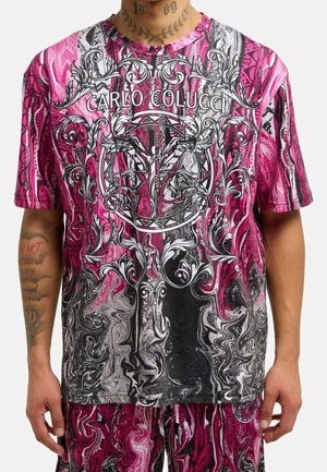 Man wears pink, black, and white marble-patterned Carlo Colucci t-shirt with ornate white and black baroque designs and matching shorts.