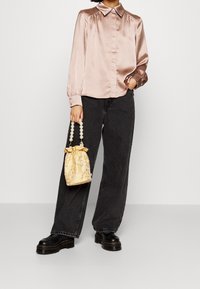 Chemise satin rose clair à manches longues avec col, associée à un jean large bleu foncé et un sac à cordon jaune à motif avec une anse en perles.