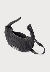 Czarna, teksturowana torba na ramię z srebrnym zamkiem błyskawicznym, regulowanym paskiem i prostokątną naszywką z logo z przodu, na jednolitym białym tle.