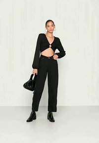 Tshirt preta cropped com mangas longas e um corte central, emparelhada com calças pretas de cintura alta e botas pretas de salto.