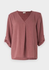 Blouse ample mauve avec un décolleté en V et des manches trois-quarts. Tissu texturé avec manches retroussables et ourlet droit.