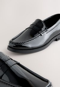 Mocassins en cuir verni noir à finition lisse, ornés de coutures décoratives et dotés d'une semelle rembourrée. Bout arrondi et design à talon bas.