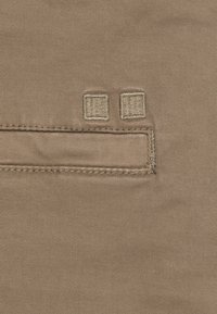 Primo piano di un tessuto beige che mostra una tasca orizzontale cucita con due piccoli dettagli a punto quadrato sopra di essa.
