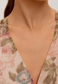 Blumiges Stoffmuster in Pastellfarben mit V-Ausschnitt. Glatte Textur mit blassen rosa, grünen und blauen Blumendetails.