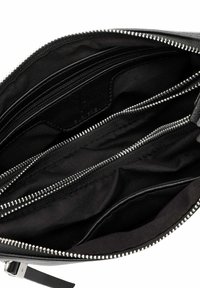 Interno di una borsa nera con zip, dotata di più scomparti, con foderatura in tessuto liscio e dettagli in zip argentati. Design organizzato.