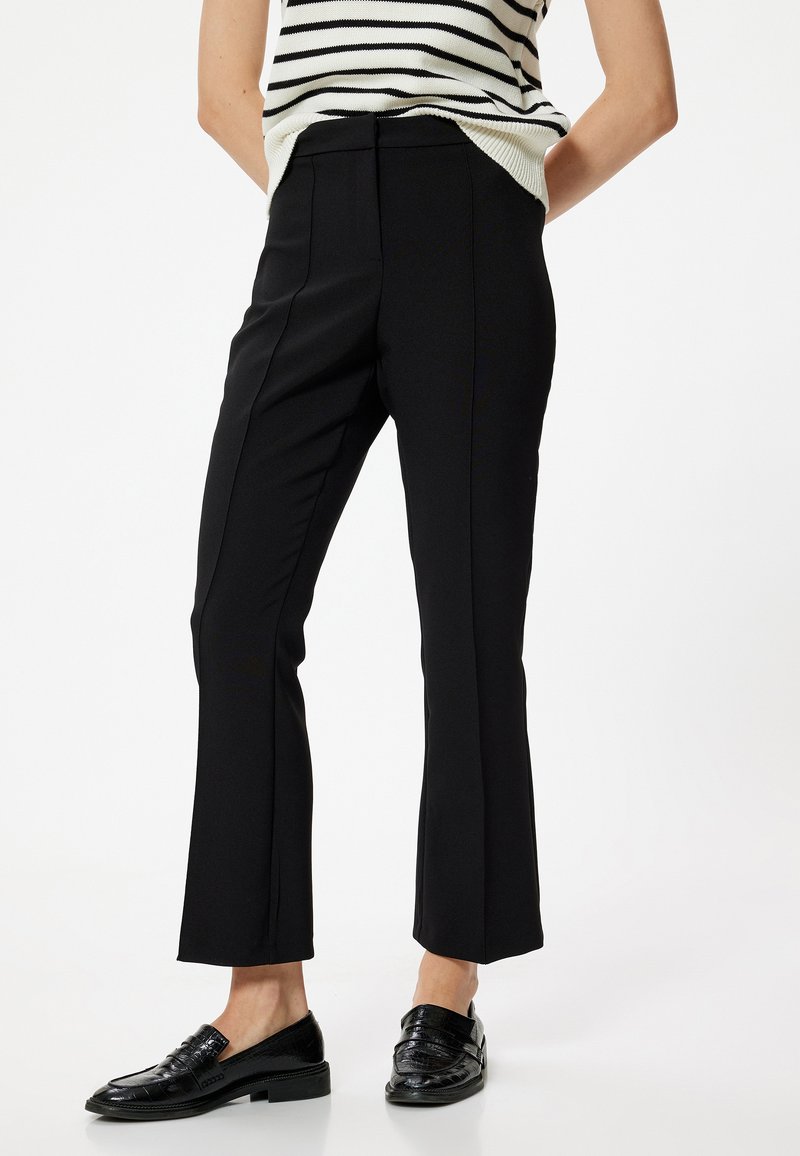 Zwarte op maat gemaakte broek met een smal figuur, gemaakt van soepel stof en met subtiele voornaden; gecombineerd met glanzende zwarte instapschoenen.
