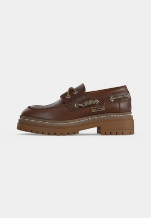 Mocassin en cuir marron avec semelle épaisse en caoutchouc, détail de lacet latéral et étiquette "Weekend" sur le côté, présenté de profil extérieur.