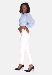Blusa corta azzurra con maniche a sbuffo, abbinata a jeans bianchi aderenti e décolleté nere a punta. Tessuto liscio e forma aderente.