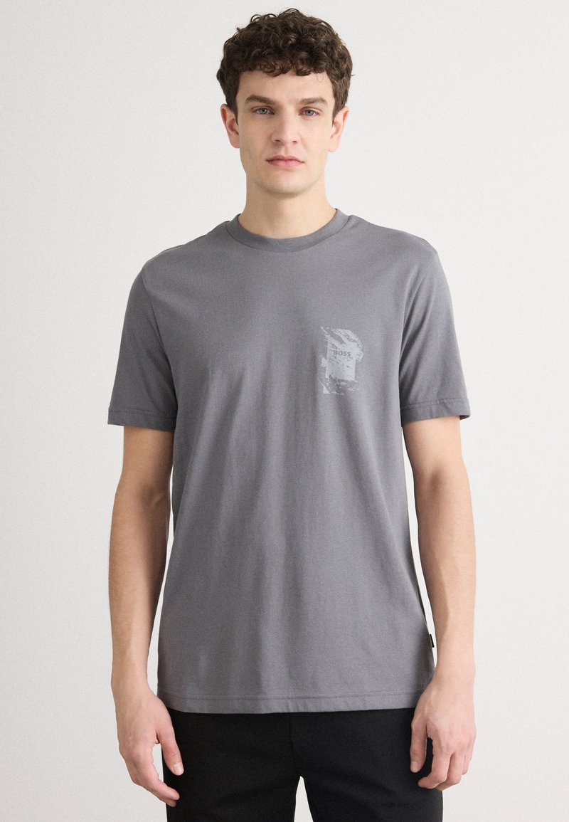 Grijze katoenen t-shirt met korte mouwen, ronde hals en een structuurafdruk op de linkerkant van de borst. Eenvoudig ontwerp, comfortabele pasvorm.
