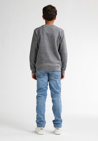 Grauer Fleece-Pullover, blaue Jeans, weiße Sneakers mit Logo. Glatte Textur, lässige Passform, sichtbare Nähte an den Jeans.