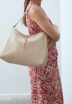 Beigenvärinen nahkainen hobo-laukku, jossa on sileä pinta, punottu sulkija ja pitkä olkahihna kantamista varten.