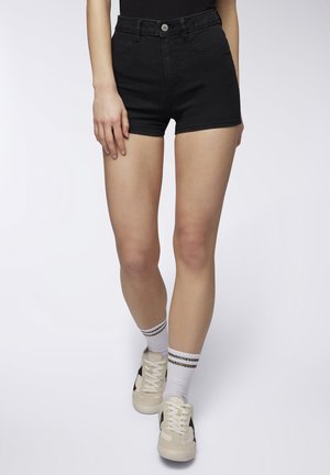 Shorts in denim neri a vita alta con un design aderente. Abbinati a calzini bianchi con righe nere e sneakers di colore chiaro. Texture liscia.