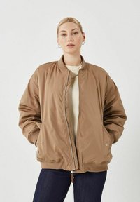 Chaqueta bomber marrón con cremalleras en la parte delantera, puños acanalados y dos bolsillos laterales. Fabricada en un material suave y ligero con un ajuste relajado.