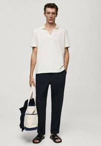 Witte textuur korte mouw polo shirt, donkere broeken, zwarte sandalen en een canvas tas met een marineblauwe accent. Eenvoudige, moderne casual outfit.
