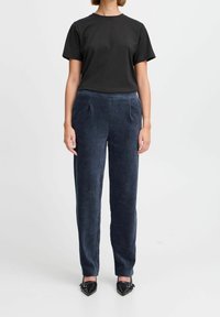 Czarna bawełniana koszulka zestawiona z granatowymi sztruksowymi spodniami. Spodnie mają delikatne pionowe paski i kieszenie. Noszone z czarnymi spiczastymi butami.