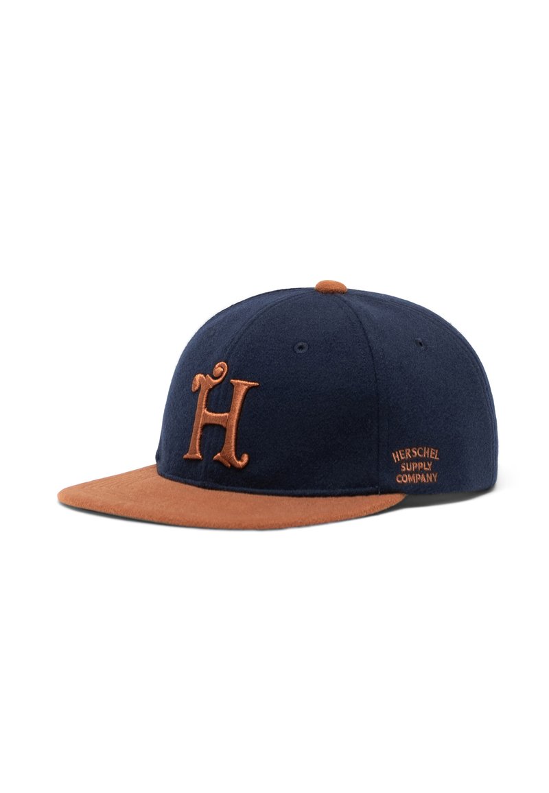 Tummansininen baseball-hattu, jossa on ruskea mokkanahkareunus. Hatussa on brodeerattu "H"-logo ruskeana ja "Herschel Supply Company" -tunnustus sivussa.