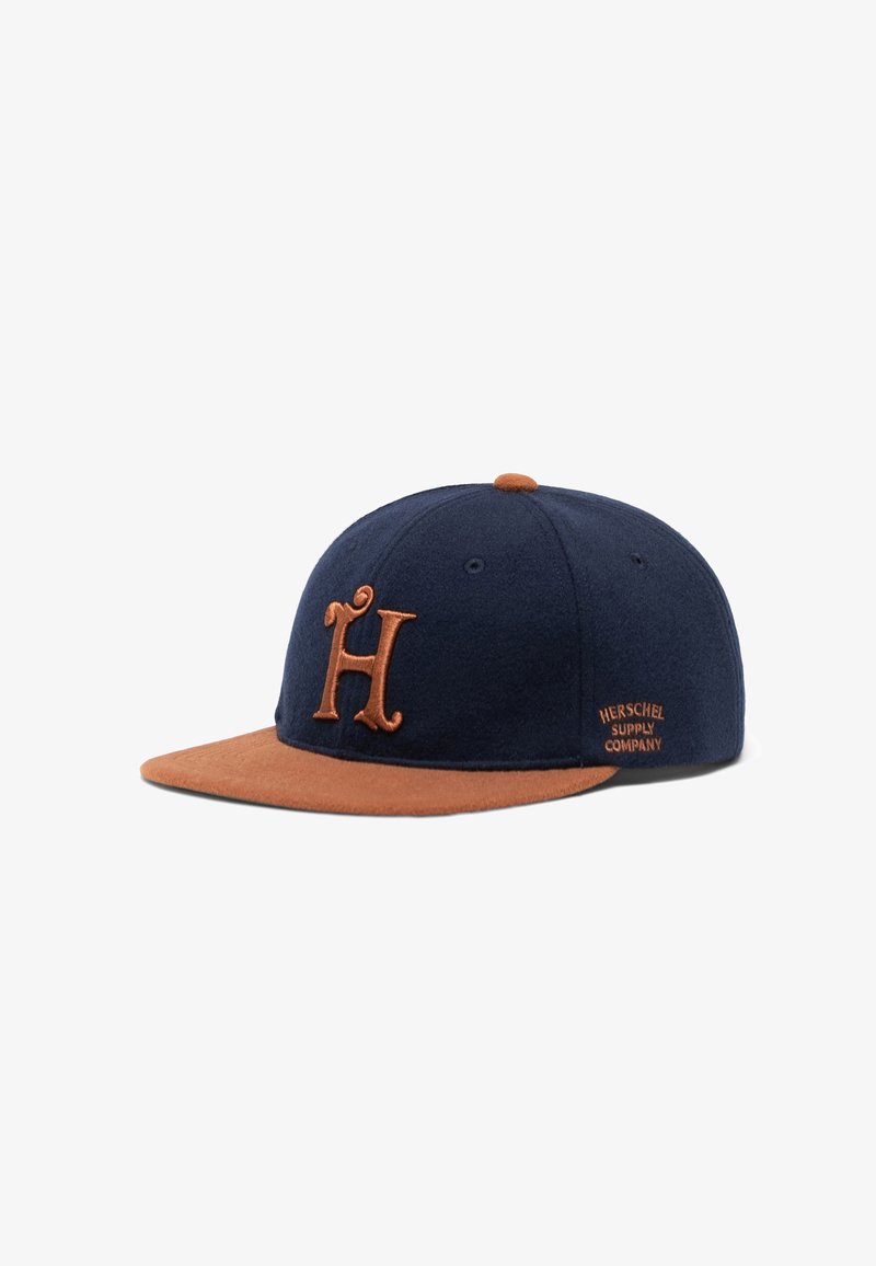 Marineblaue Baseballmütze mit braunem Wildledervisier, ausgestattet mit einem gestickten "H"-Logo in Braun und einem "Herschel Supply Company"-Tag an der Seite.