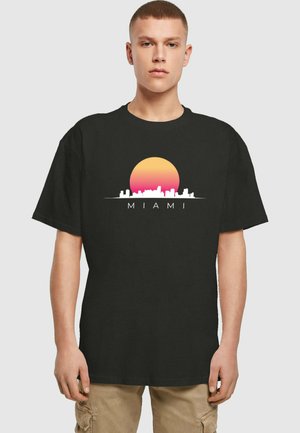 T-shirt in cotone nero con una grafica di un tramonto e una silhouette dello skyline con la scritta "MIAMI" in bianco. Maniche corte, vestibilità rilassata.