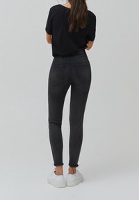 Musta skinny-farkut, joissa on sileä pinta, rispaantunut lahkeenreuna ja kaksi takataskua, yhdistettynä valkoisiin lenkkareihin ja mustaan t-paitaan.