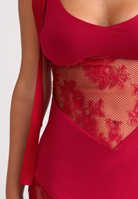 Zbliżenie czerwonej sukienki z kwiatowym panelem z koronki siatkowej na wysokości talii oraz gładką tkaniną na biuście i dole talii.