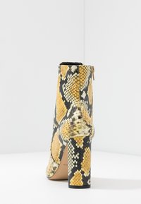 Bottine en cuir effet peau de serpent avec un motif jaune et noir, surface texturée, et un talon bloc haut. Dispose d'une fermeture éclair dorée à l'arrière.