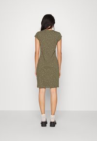 Oliwkowa sukienka z krótkim rękawem w kwiatowy wzór. Dopasowany krój sięga powyżej kolan, w połączeniu z wzorzystymi skarpetkami i butami na słupku.