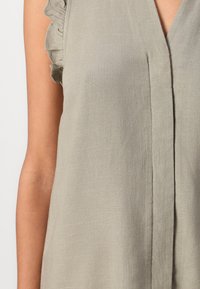 Top senza maniche grigio chiaro con scollatura a V, caratterizzato da dettagli arricciati sulle spalle e un tessuto leggermente strutturato.