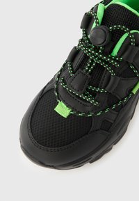 Μαύρο αθλητικό παπούτσι με πλέγμα και συνθετικά υλικά. Διαθέτει νεον πράσινα στοιχεία και σύστημα κορδονιών με κούμπωμα για ασφαλή εφαρμογή. Υφή με ανάγλυφη επιφάνεια.