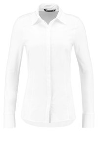 Camicia bianca a maniche lunghe con colletto a punta, vestibilità sartoriale, cuciture pronunciate e orlo dritto. Tessuto liscio e leggero.