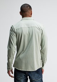 Lichtgroen overhemd met lange mouwen, een kraag en knoopmanchetten, gemaakt van een soepele stof, gecombineerd met donkerblauwe jeans.