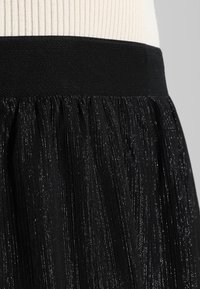 Jupe noire avec une large taille, un design fluide et une finition texturée avec des fils métalliques, créant un effet de scintillement subtil.