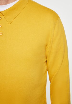 Pulover polo tricotat galben, cu guler, închidere cu trei nasturi și textură elastică. Perspectiva de aproape evidențiază țesătura.