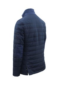 Giacca trapuntata blu navy con colletto alto, toppe testurizzate sui gomiti e spacchi laterali. Realizzata in tessuto liscio e leggero.