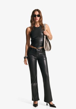 Černý kožený crop top a kalhoty do zvonu, s hladkou texturou. Doplňky zahrnují černé sluneční brýle a stříbrnou ramenní tašku.