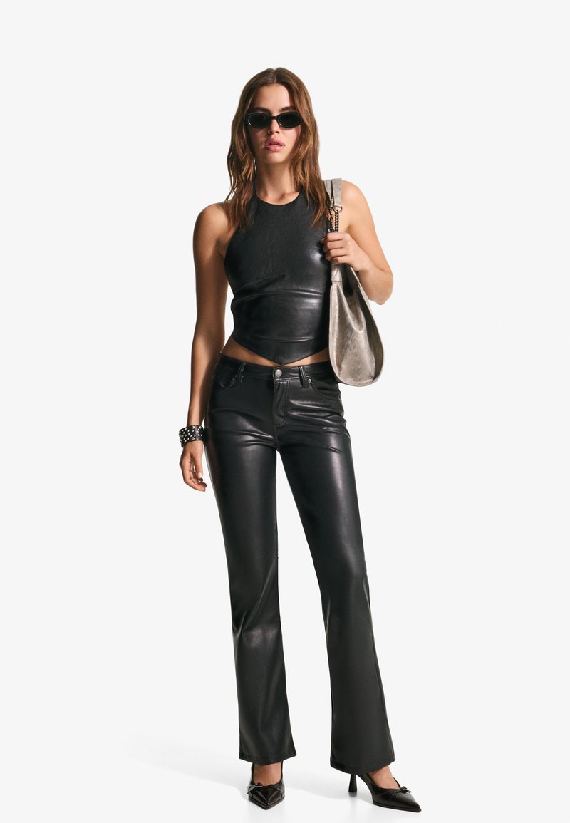 Top scurt din piele neagră și pantaloni evazați, cu o textură netedă. Accesoriile includ ochelari de soare negri și o geantă argintie de umăr.