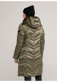 Olijfgroene pufferjas met een capuchon, een chevron-quiltpatroon en lange mouwen. Zwart accent op de linkermouw.