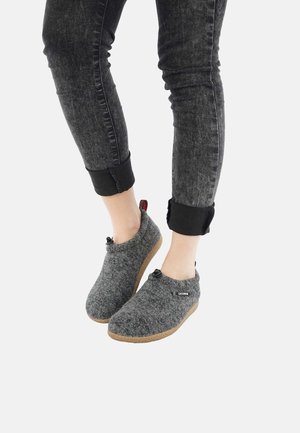 Gray felt slippers with a rounded shape, rubber soles, and decorative buttons, worn with dark jeans rolled at the cuffs.
