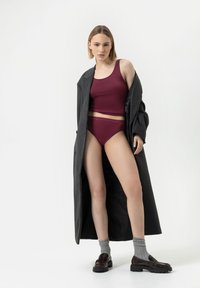 Bordowy top na ramiączkach i wysokie majtki połączone z długim szarym płaszczem, szarymi skarpetkami i brązowymi mokasynami. Gładkie tekstury i dopasowany krój.