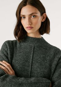 Sweater tricotado cinza escuro com um colarinho alto canelado, apresentando um tecido texturizado, mangas longas e um corte reto.