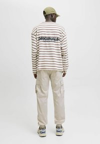 Gestreiftes Langarmshirt in Beige und Braun mit dem Schriftzug "ORIGINALS". Kombiniert mit hellen Cargohosen und Turnschuhen.