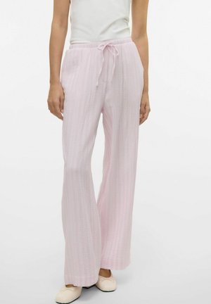 Pantalons larges rose clair en tissu texturé avec une taille à cordon. Associés à un haut blanc ajusté et des chaussures crème.