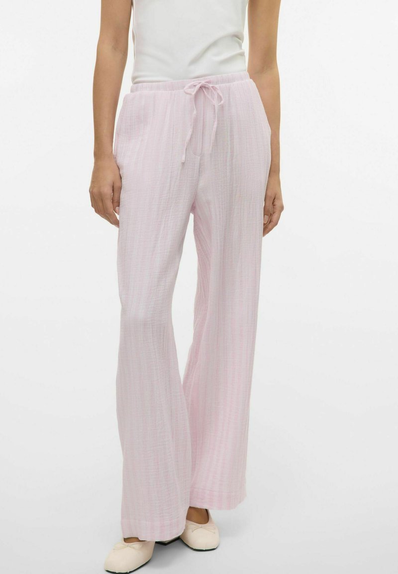 Ljusrosa, vida byxor med textilstruktur och dragsko i midjan. Stylad med en åtsittande vit topp och krämfärgade skor.