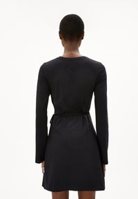 Zwarte lange mouwen jurk gemaakt van zachte stof, met een ronde halslijn, een gestrikte taille en een rechte silhouet. Minimalistisch design zonder patronen.