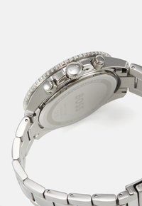 Orologio in acciaio inossidabile argento con un quadrante testurizzato, tre pulsanti di corona e un bracciale a maglie. Mostra la scritta "BOSS" sul lato e sul retro.