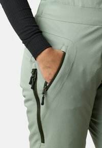 Ljusgröna utomhusbyxor har zippered sidofickor, en slät yta och en figurnära design, i kombination med en svart ribbad långärmad topp.