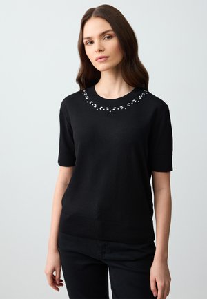 Maglione nero a maniche corte con scollo rotondo, caratterizzato da dettagli di perline decorative lungo il collo; texture a maglia liscia e design aderente.