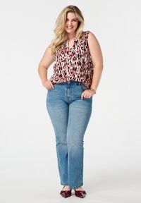 Top sans manches, de couleur rose clair avec un motif rouge, associé à un jean bleu taille haute ; le mannequin porte des ballerines bordeaux ; fond neutre.