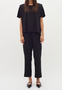 Svart, kortärmad topp i kombination med svarta, vida byxor. Båda plaggen har en slät tygkvalitet och minimalistisk design. Spetsiga skor.