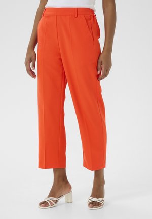 Orange, tailored trousers with a high waist, pleats, and a wide leg design. Fabric is smooth; features side pockets. Paired with white heeled sandals.