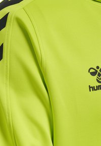Fluoreszierendes gelbes Sportshirt mit schwarzen Akzenten, ausgestattet mit glattem Stoff, einem Rundhalsausschnitt und einem Logo auf der Brust.